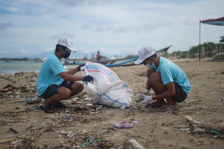 a man sitting on top of a sandy beach doing a beach clean up